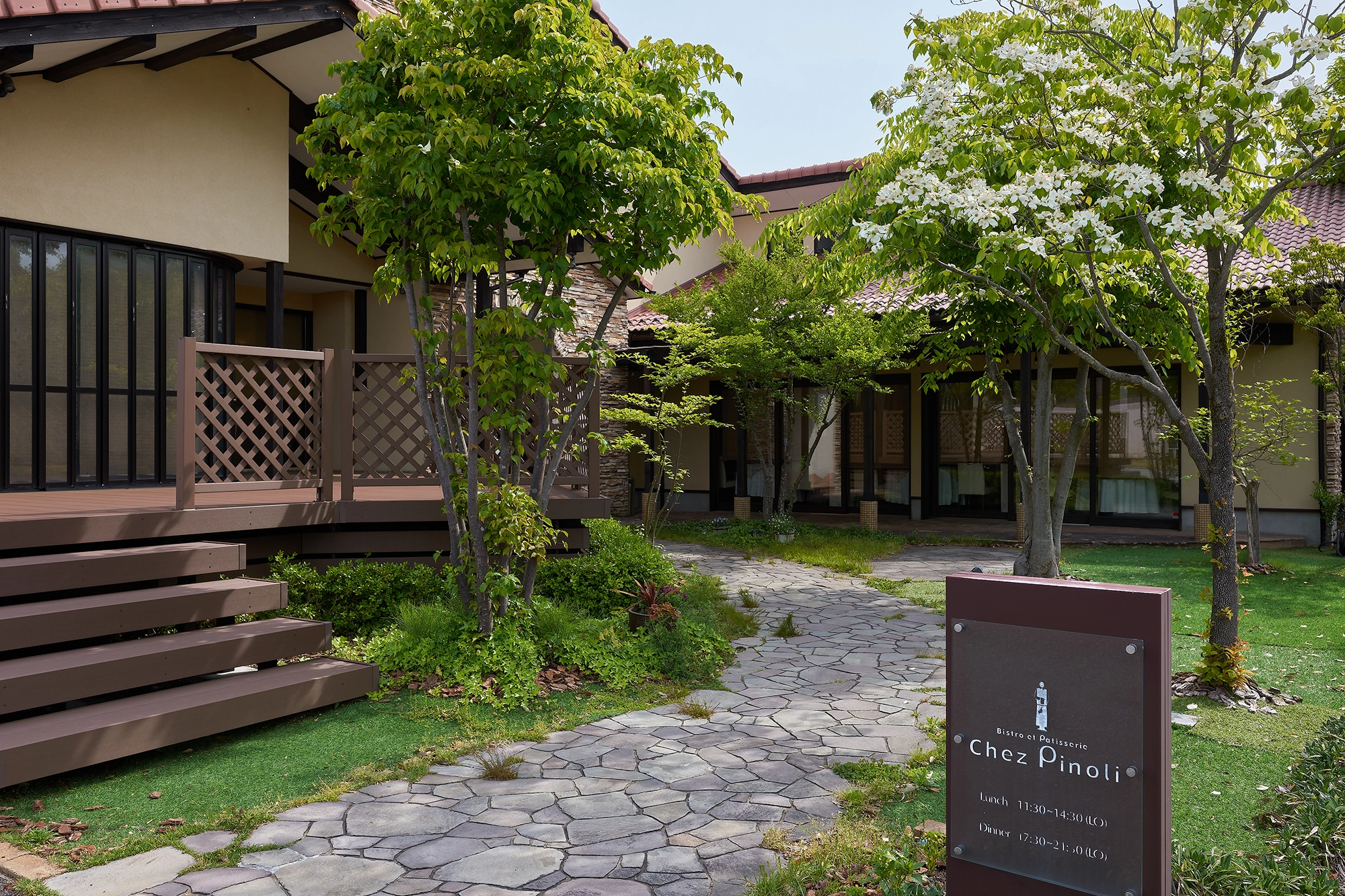 シェ・ピノリの看板と緑に囲まれたアプローチ